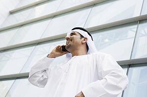 Businessman standing outdoors by building on cellular phone smiling (selective focus)