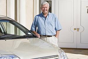 Senior man standing with his car outside his home