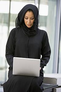 Businesswoman sitting outdoors with laptop by building (selective focus)