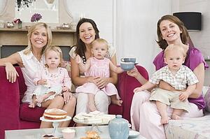 Three mothers in living room with babies and coffee smiling