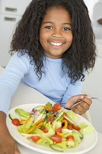Young girl in kitchen eating salad smiling