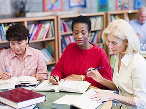 Three women sitting in library with books and notepads (selective focus)