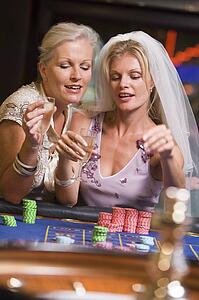 Woman in bridal veil with another woman in casino playing roulette and smiling (selective focus)