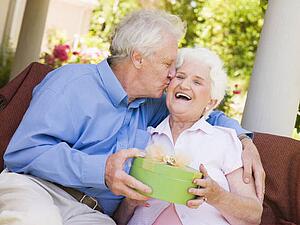 Husband giving wife gift on patio kissing her and smiling