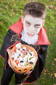Young boy outdoors wearing vampire costume on Halloween holding candy