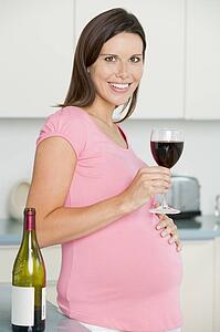 Pregnant woman in kitchen with glass of red wine smiling