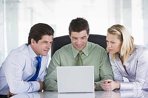Three businesspeople in a boardroom looking at laptop