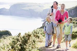 Family walking on cliffside path holding hands and smiling