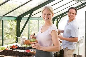 Couple in greenhouse raking soil in pots smiling