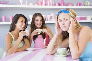 Young woman with a hangover sitting at a table with two friends