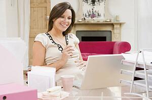 Pregnant woman in home office with laptop eating and smiling