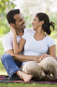 Couple sitting outdoors in park being affectionate and smiling (selective focus)
