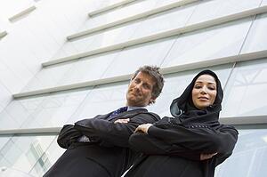 Two businesspeople standing outdoors by building smiling (high key/selective focus)