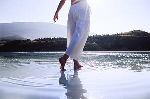 Woman's legs outdoors walking on water in scenic location (lens flare)