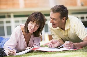 Adult students lying on lawn of school studying and talking