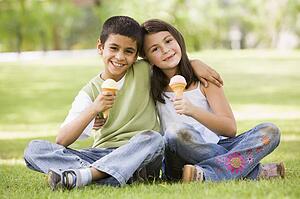 Two young children outdoors in park with ice cream smiling (selective focus)
