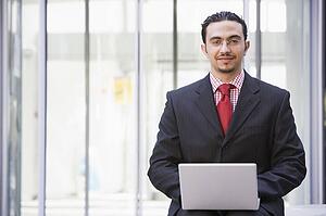 Businessman sitting outdoors by building with a laptop smiling (high key/selective focus)