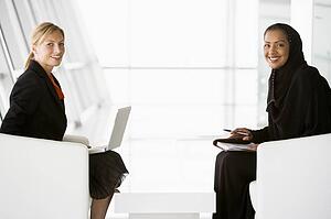 Two businesswomen indoors with a laptop smiling (high key/selective focus)