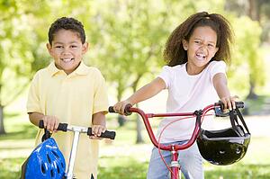 Brother and sister outdoors with scooter and bicycle smiling