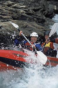 Two kayakers rowing in rapids and smiling