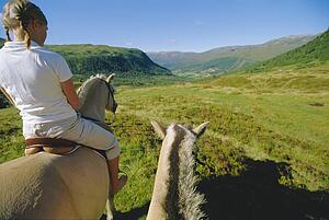 Woman outdoors riding horse in scenic location with another horse beside her