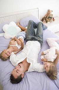 Man lying in bed with two young girls smiling