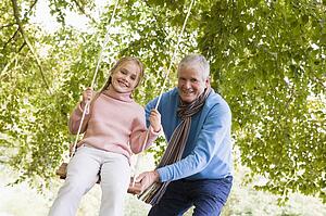 Grandfather pushing granddaughter on swing and smiling (selective focus)