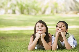 Two young children outdoors lying in park smiling (selective focus)