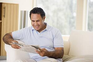 Man relaxing with newspaper in living room and smiling