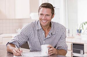 Man in kitchen reading newspaper and smiling