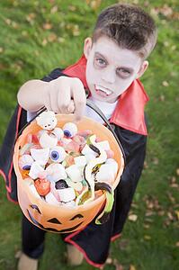 Young boy outdoors wearing vampire costume on Halloween holding candy
