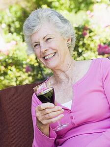 Senior woman sitting outdoors on a chair with a glass of red wine
