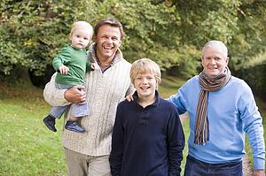 Two men and two young children standing on path outdoors smiling (selective focus)