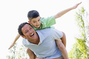 Man giving young boy piggyback ride outdoors smiling