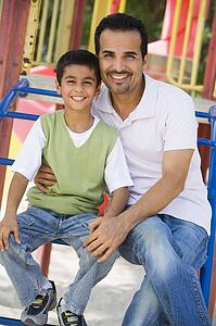Father and son sitting on playground structure smiling (selective focus)