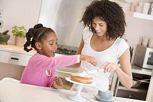Woman and young girl in kitchen icing a cake smiling