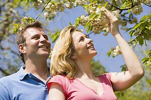Couple standing outdoors holding blossom smiling