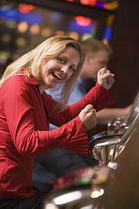 Woman in casino excited playing slot machine with people in background (selective focus)