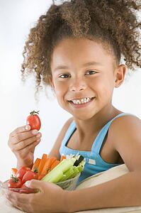 Young girl eating bowl of vegetables in living room smiling