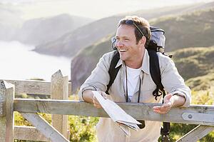 Man relaxing on cliffside path holding map and laughing