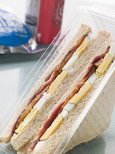 Egg And Bacon Sandwich On White Bread With A Bag Of Crisps And A Can Of Fizzy Drink