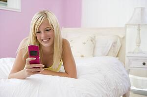 Teenage Girl Lying On Bed Using Mobile Phone 