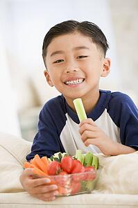 Young boy eating bowl of vegetables in living room smiling