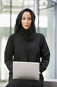 Businesswoman sitting outdoors with laptop by building (selective focus)