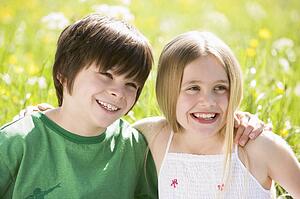Two young children sitting outdoors arm in arm smiling