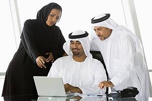 Three businesspeople in office with laptop pointing and smiling (high key/selective focus)