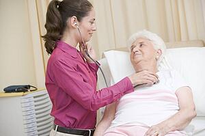 Doctor giving checkup with stethoscope to woman in exam room smiling