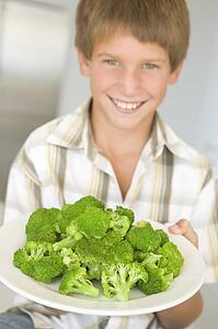 Young boy in kitchen eating broccoli smiling