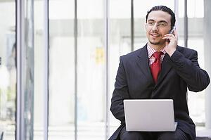Businessman sitting outdoors by building with a laptop on cellular phone (high key/selective focus)