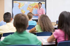 Students in class with teacher at front showing map (selective focus)